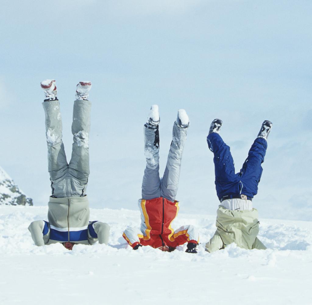 group of three friends doing head stand in snow